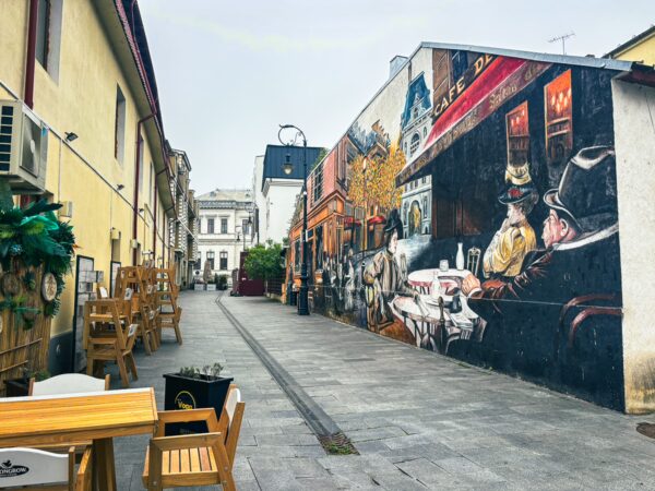 Vibrant street art decorates a wall in the old town, with cozy outdoor seating showcasing the charm of Craiova, Romania.
