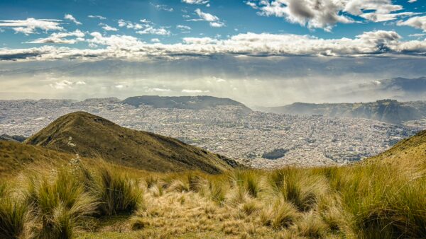Lush grasslands lead to stunning views over Quito from Pichincha Volcano, showcasing a vibrant cityscape under dramatic skies.