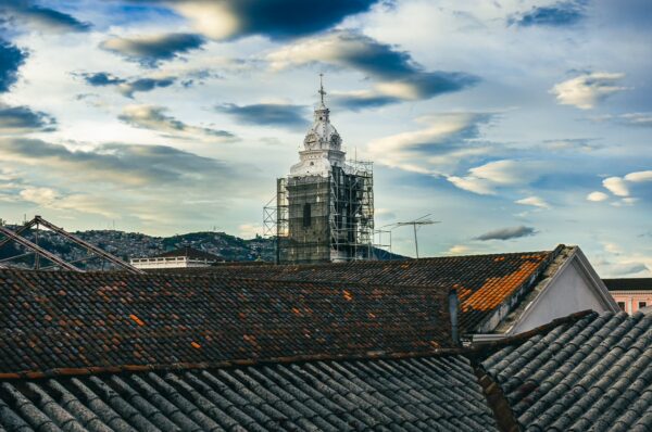 View from Hostal Yumbo showcases a historic tower draped in scaffolding against a dramatic sky in Quito, Ecuador.