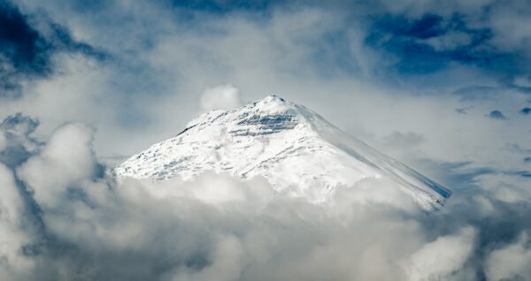 Snow-capped Cotopaxi peak rises majestically above swirling clouds in Cotopaxi National Park, Ecuador.