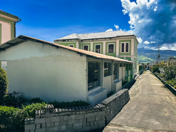 Charming green and white buildings line a quiet street in Machachi, Ecuador, under a bright blue sky and scattered clouds.