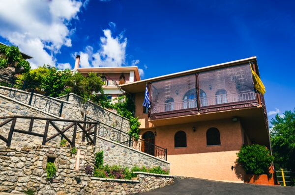 Panagia Kernitsis Monastery features a charming stone facade and vibrant greenery under a bright blue sky in Arcadia, Greece.