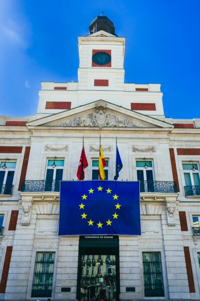 Puerta del Sol features a historic building with vibrant European Union flags, surrounded by a clear blue sky in Madrid, Spain.