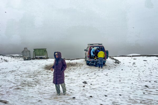 Refugio Carrel at Chimborazo Volcano features snow-covered terrain, a visitor in a purple jacket, and a parked vehicle in Ecuador.