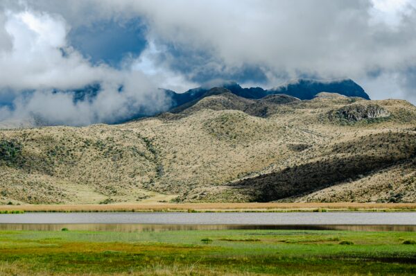 Lush green hills and a tranquil lake reflect the dramatic clouds above in Cotopaxi National Park, Ecuador.