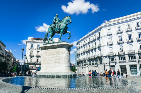 Equestrian statue of Carlos III stands proudly in a plaza, surrounded by historic buildings and a clear blue sky in Madrid, Spain.