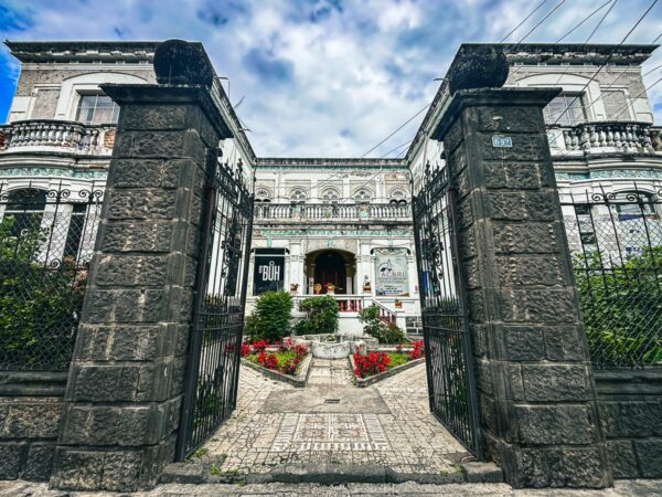 Elegant colonial mansion with vibrant gardens in Ibarra, Ecuador, framed by stone gates and a dramatic sky.