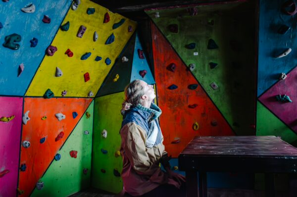 Vibrant climbing wall with colorful holds and a person sitting at a table, inside the José Rivas Refuge, Mount Cotopaxi, Ecuador.