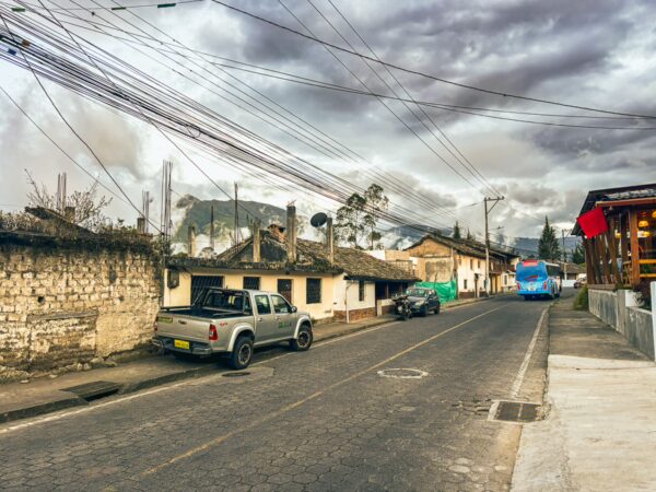 Quiet street in La Esperanza, Ibarra, Ecuador, featuring traditional buildings, power lines, and a parked truck under gray skies.