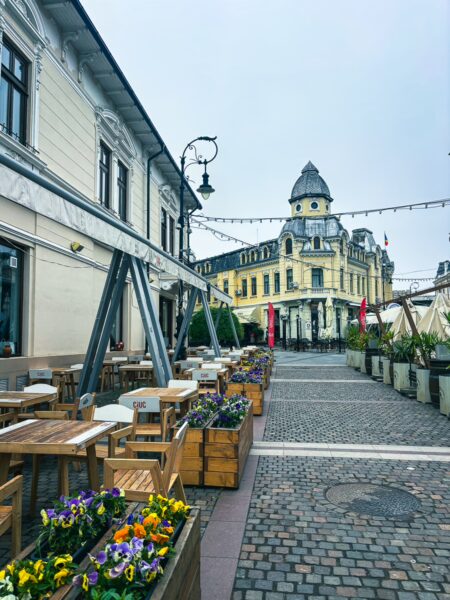 Charming cobblestone street featuring outdoor dining, vibrant flower boxes, and historic architecture in Old Town Craiova, Romania.