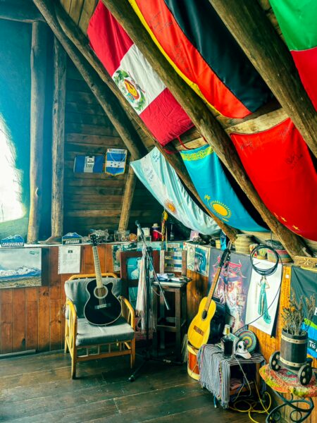 Cozy interior of Rey Venture restaurant lodge, featuring guitars, colorful flags, and wooden beams in Machachi to Chimborazo, Ecuador.