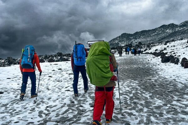 Hikers with colorful gear trekking on a snowy trail toward Chimborazo Volcano in Ecuador, under a cloudy sky.