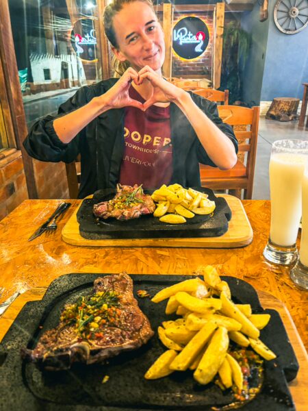Enjoying sizzling steak and golden potatoes at a restaurant in La Esperanza, Ibarra, Ecuador, with a heart gesture.