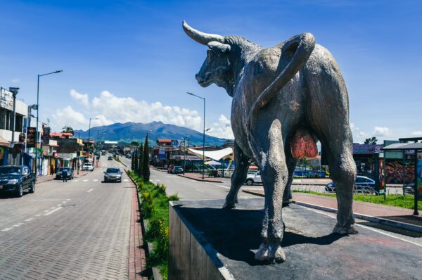 Silver bull statue stands prominently along the street in Machachi, Ecuador, with mountains visible in the background.