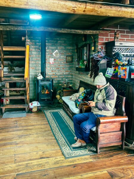 Cozy interior of Rey Venture Restaurant Lodge in Machachi, Ecuador, featuring a warm timber setup and a guest relaxing on a wooden sofa.