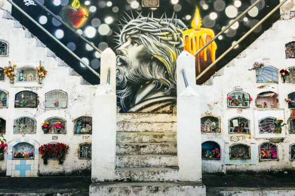 Colorful mural of a crowned figure in a cemetery, featuring white tombs adorned with flowers in Tulcán, Ecuador.