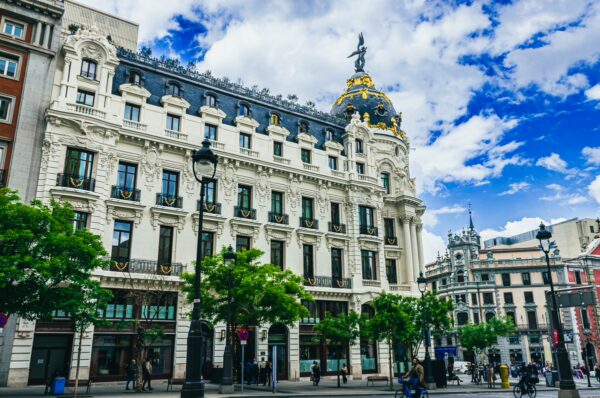 Elegant architecture in Madrid, Spain, featuring intricate details and lush green trees under a vibrant sky.