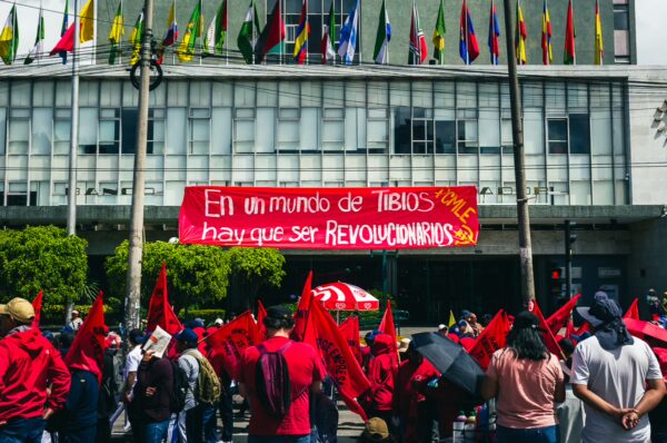 Red flags and banners fill the streets during the International Workers' Day parade in Quito, Ecuador, vibrant with protest energy.