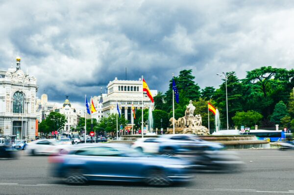 Cibeles Fountain with flowing water, surrounded by flags and greenery, set against a dramatic cloudy sky in Madrid, Spain.