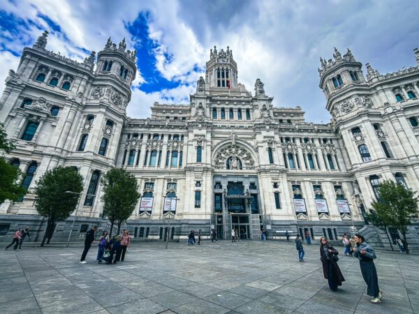 Imposing architecture of Portico de los Buzones in Madrid, showcasing intricate details and lively visitors against a dramatic sky.