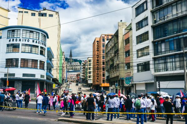 Vibrant International Workers' Day parade in Quito, Ecuador, with crowds holding flags and colorful buildings lining the street.