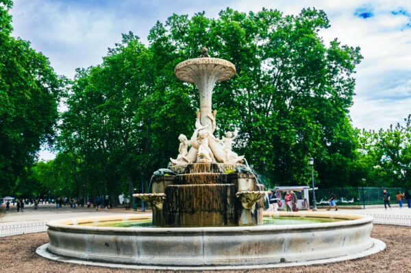Elegant fountain surrounded by lush greenery in Parque El Retiro, Madrid, Spain, with visitors enjoying the serene atmosphere.