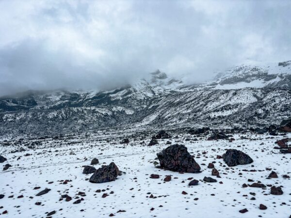Snow-covered landscape with rocky terrain and cloudy skies at Chimborazo Volcano, Ecuador.