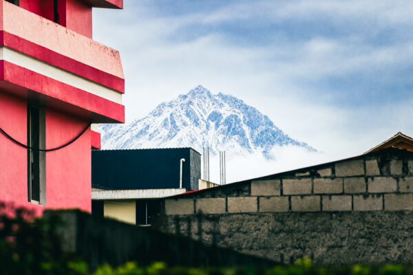 Snow-capped Iliniza Sur volcano rises majestically behind urban buildings in Machachi, Ecuador, under a cloudy sky.