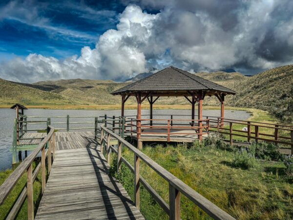 Stunning view of Laguna de Limpiopungo with a rustic gazebo and wooden walkway amid lush green hills in Cotopaxi National Park, Ecuador.
