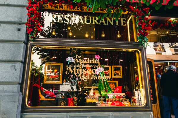 Vibrant storefront of Museo del Jamón in Madrid, featuring colorful displays of hams and festive decorations.