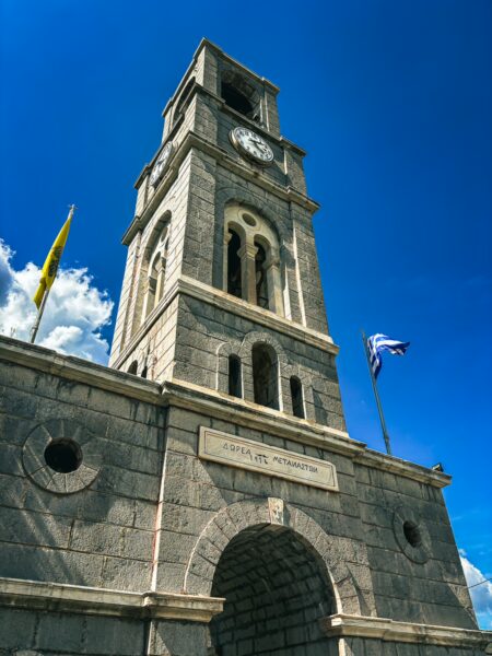 Towering clock tower in Nymfasia, Arcadia, Greece, showcases stunning stone architecture against a vibrant blue sky.