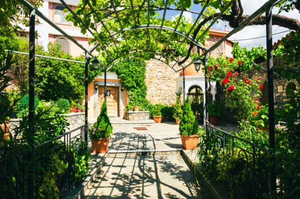 Lush greenery frames the tranquil courtyard of Panagia Kernitsis Monastery in Arcadia, Greece, blooming with vibrant flowers.