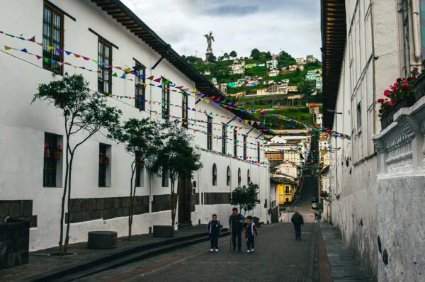 Colorful prayer flags decorate the narrow street in Quito, Ecuador, leading to a hillside with vibrant buildings and greenery.