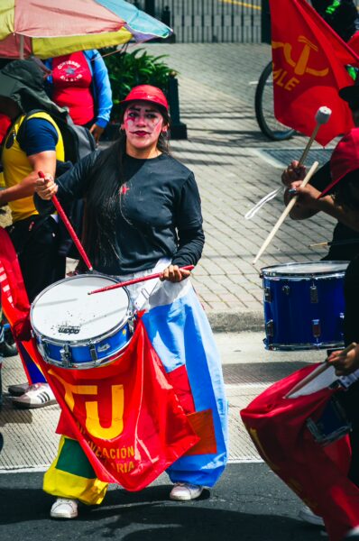 Vibrant drummers celebrate International Workers' Day in Quito, Ecuador, with colorful banners and lively attire.
