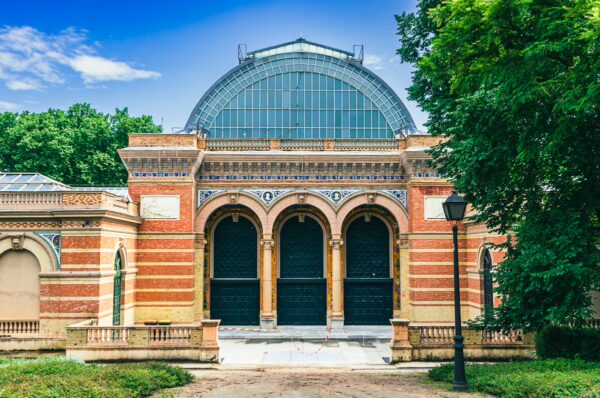 Brick and glass conservatory featuring arched entrances, surrounded by green trees in Parque El Retiro, Madrid.