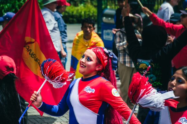Colorful parade participants celebrate International Workers' Day in Quito, Ecuador, holding flags and cheering joyfully.