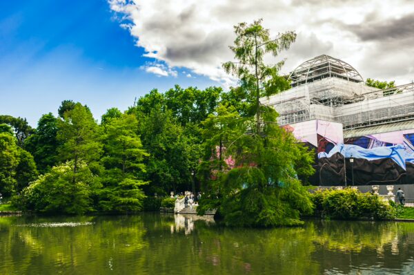 Lush greenery surrounds a tranquil lake at Parque El Retiro in Madrid, Spain, with a backdrop of a partially constructed building.