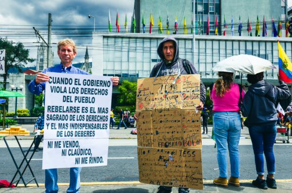 Two protesters hold signs during the International Workers' Day parade in Quito, Ecuador, highlighting rights and government issues.
