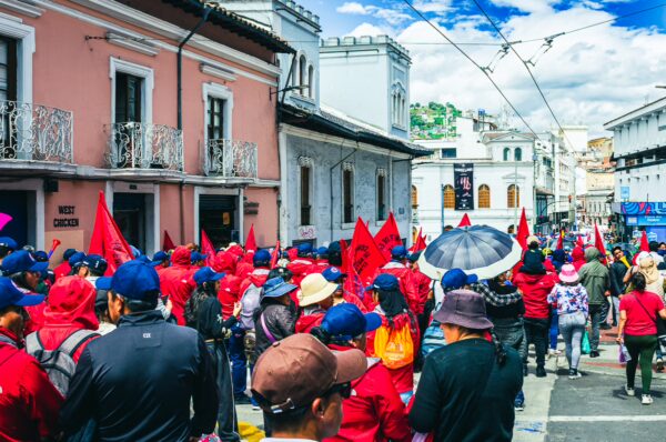 Participants in a vibrant red-clad parade celebrating International Workers' Day in Quito, Ecuador, with colorful umbrellas and a festive atmosphere.