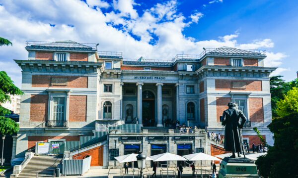 Museo del Prado features impressive architecture with a grand staircase, surrounded by greenery and a blue sky in Madrid, Spain.