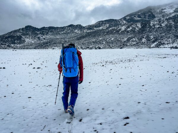 Hiker in a blue jacket and backpack walks through snow-covered terrain near Chimborazo Volcano in Ecuador.