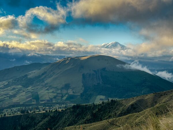 Lush green slopes of Imbabura Volcano rise under a blue sky with wispy clouds, showcasing Ecuador's stunning landscape.