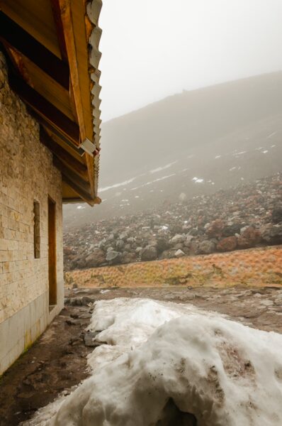 Snow-covered ground and rocky terrain near the José Rivas Refuge, shrouded in mist on Mount Cotopaxi, Ecuador.