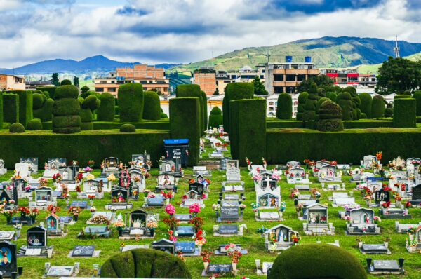 Colorful graves dot the lush green landscape of Tulcán Cemetery, framed by neatly trimmed hedges and dramatic clouds in Ecuador.