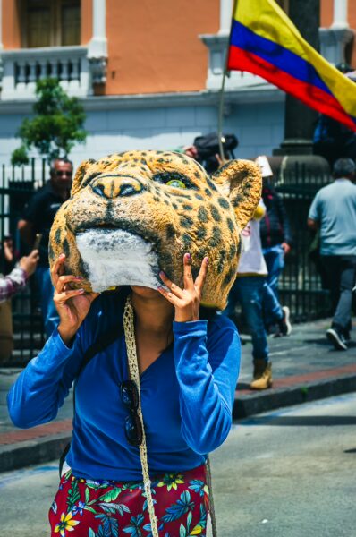 Colorful participant wearing a leopard mask at the International Workers' Day parade in Quito, Ecuador, celebrating local culture.