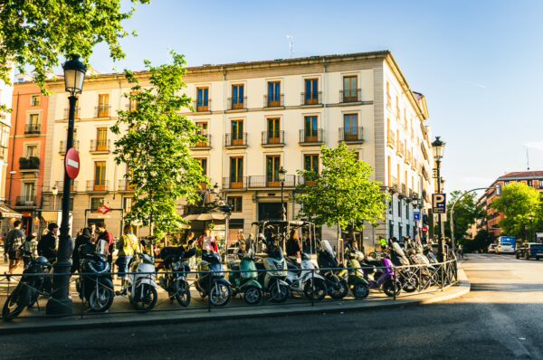 Bicycles line the street in Madrid, Spain, with sunlight reflecting off the classic architecture and vibrant green trees.