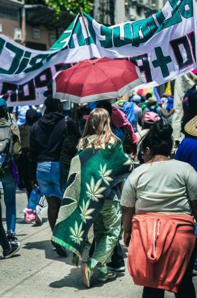 Crowd celebrating International Workers' Day in Quito, Ecuador, with colorful banners and individuals in vibrant attire and blankets.