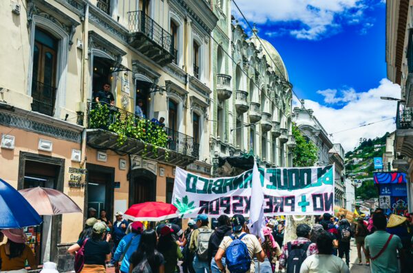 Vibrant crowd marches with banners during International Workers' Day in Quito, Ecuador, colorful umbrellas dotting the street.