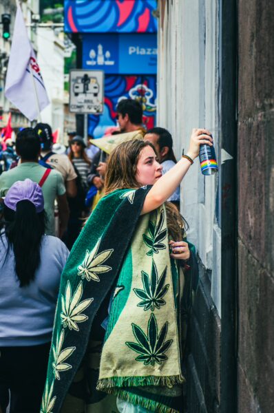 A woman in a green and patterned cloak sprays graffiti during the International Workers' Day parade in Quito, Ecuador.