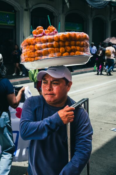 A vendor carries a tray of orange pastries on his head while walking through the International Workers' Day parade in Quito, Ecuador.